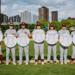 Minneapolis Roosevelt Teddy Baseball Seniors pose together holding a Baseball sign with their name on it. They stand in the infield of Parade Stadium with downtown Minneapolis buildings behind them during golden hour