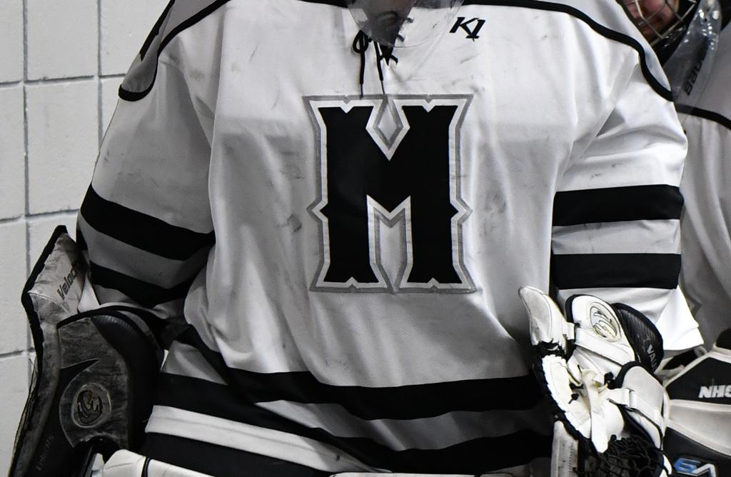 Image of Minneapolis Girls High School Hockey goalie jersey close up. a Big M logo visible - black text with a white outlline on white uniform fabric.